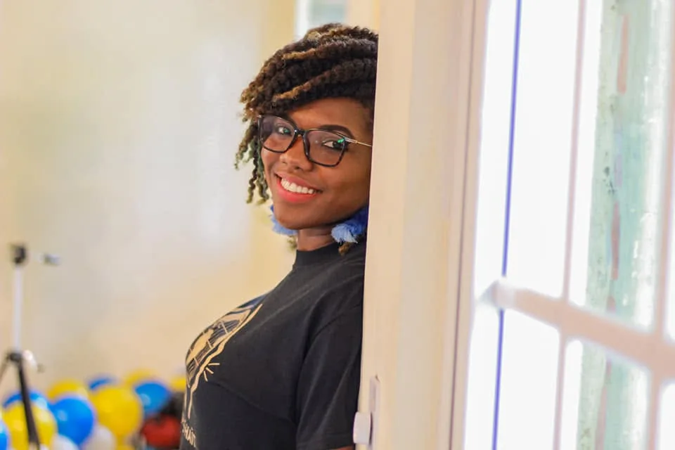 Une membre d'ADIS-HAÏTI souriante, appuyée contre un mur près d'une fenêtre