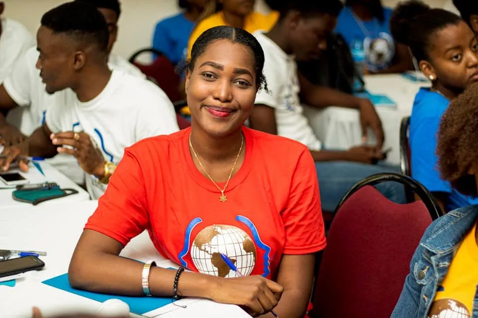 Une participante souriante en t-shirt rouge ADIS-HAÏTI, assise à une table pendant une formation