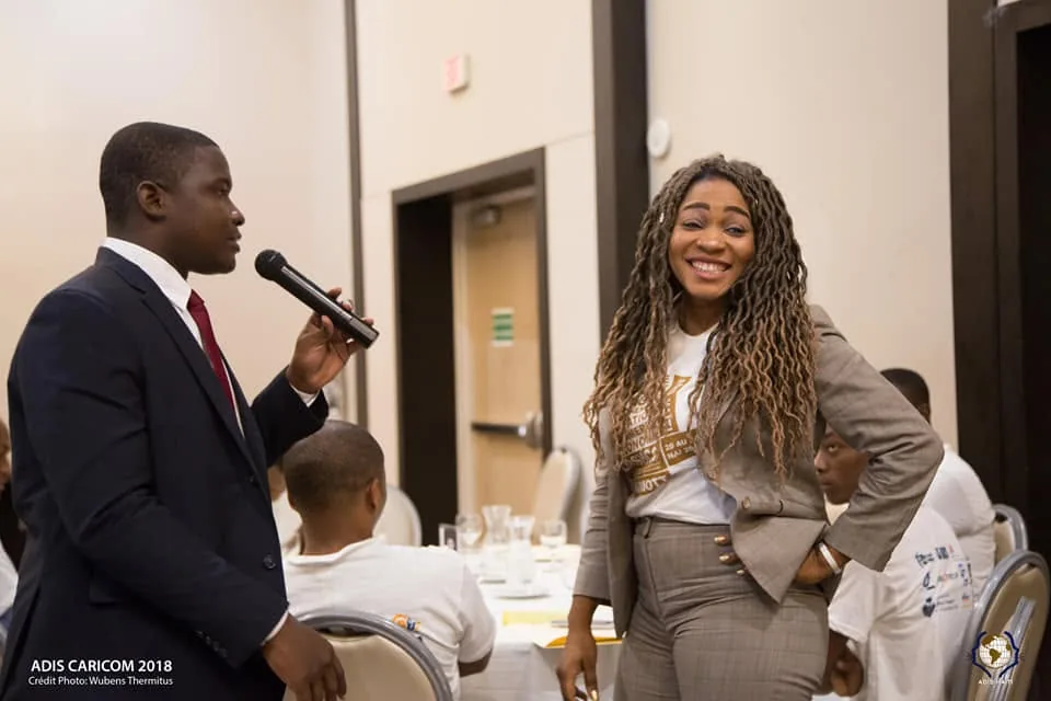 Un participant en costume prend la parole au micro à côté d'une intervenante souriante, lors d'ADIS CARICOM 2018