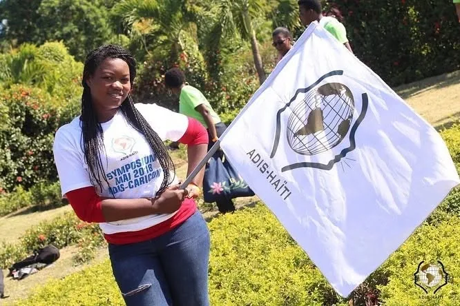 Une participante tient le drapeau blanc d'ADIS-HAÏTI dans un jardin, lors du symposium ADIS-CARICOM de mai 2018