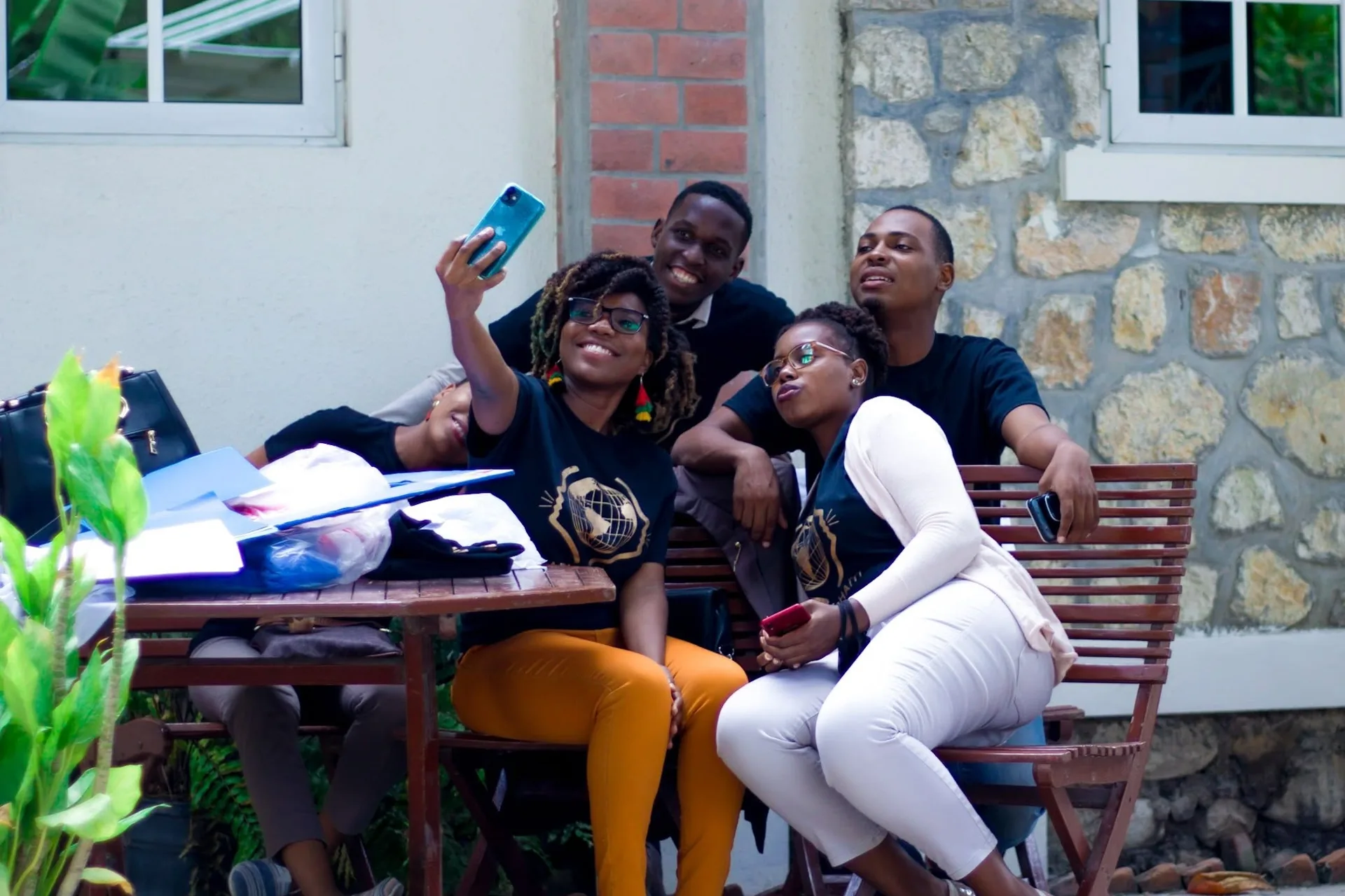 Cinq membres d'ADIS-HAÏTI en t-shirt de l'organisation prennent un selfie, assis autour d'une table en terrasse