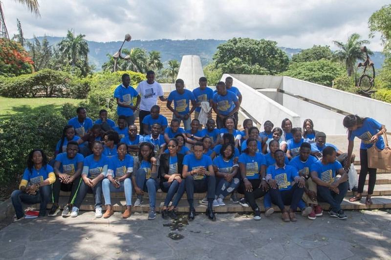 Grand groupe de membres d'ADIS-HAÏTI en tenue ARSHOEA, réunis sur les marches d'un site patrimonial