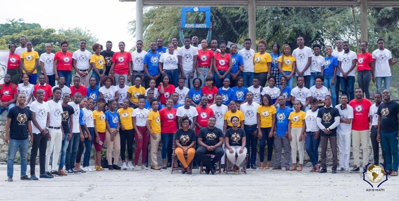 Grand rassemblement des membres d'ADIS-HAÏTI, environ soixante-dix jeunes réunis en plein air autour d'une pancarte ADIS-HAÏTI