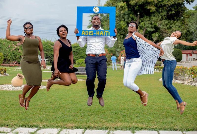 Cinq membres d'ADIS-HAÏTI sautant de joie en tenant le cadre photo ADIS-HAÏTI, dans un jardin